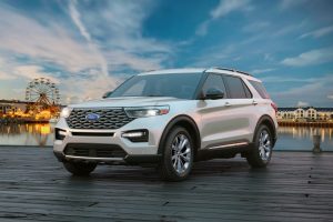 Silver 2021 Ford Explorer parked in front of festival grounds with a Ferris wheel in the background.